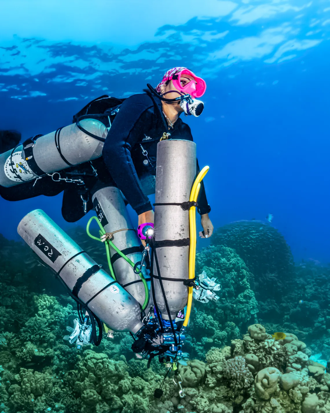 Technical diver carrying stage cylinders over a Red Sea reef